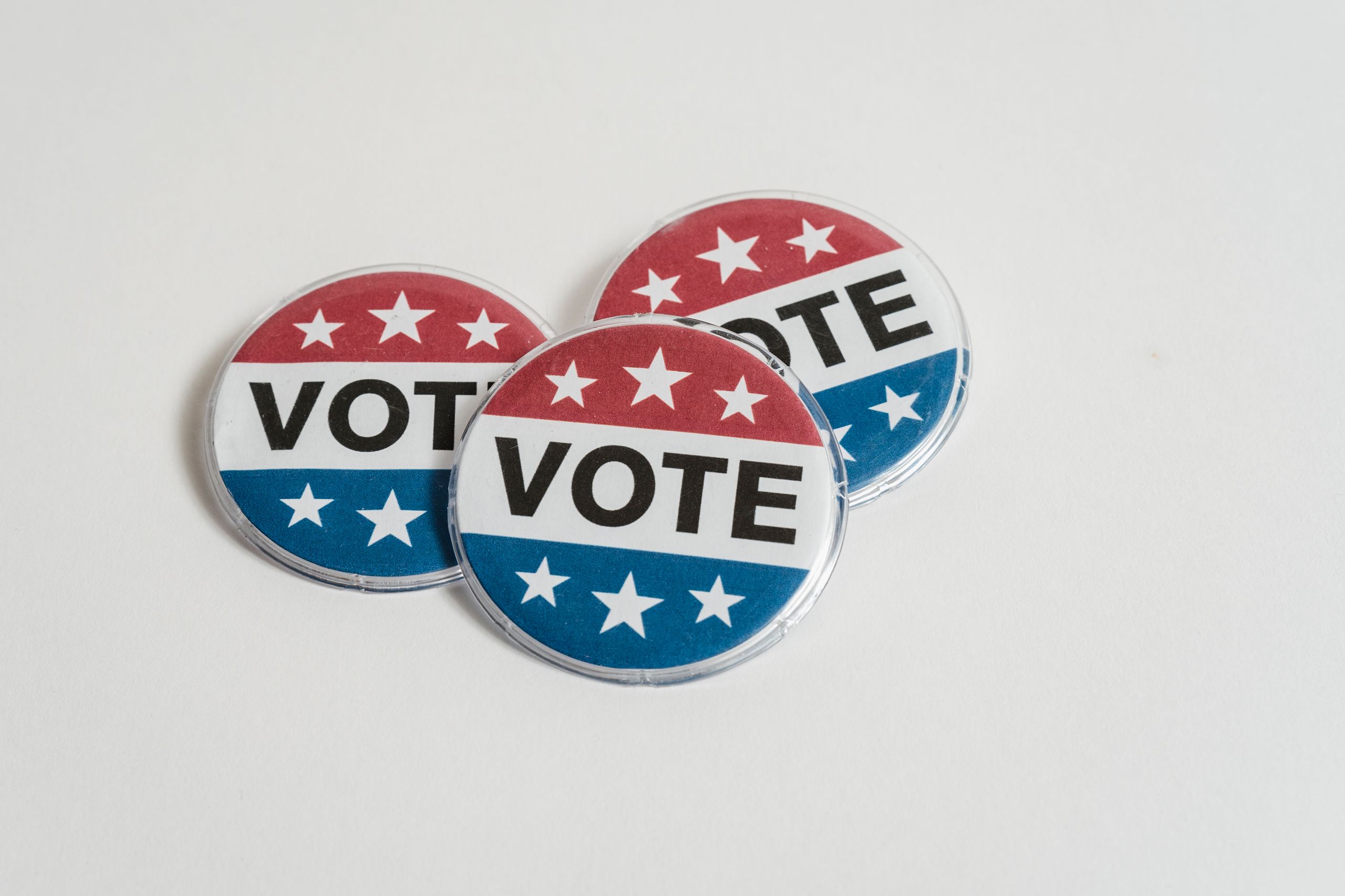 Red, white, and blue voting badges promoting elections on a clean white background.